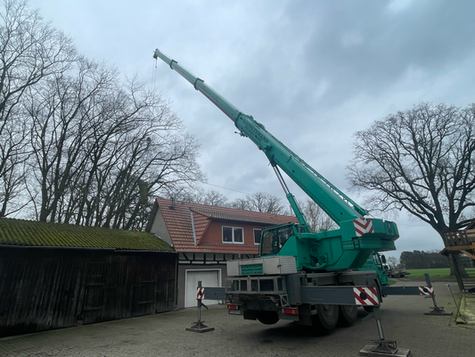 Mobilkran mit aufgefahrenem Ausleger steht auf dem Hof und arbeitet über Hausdach und Scheune.